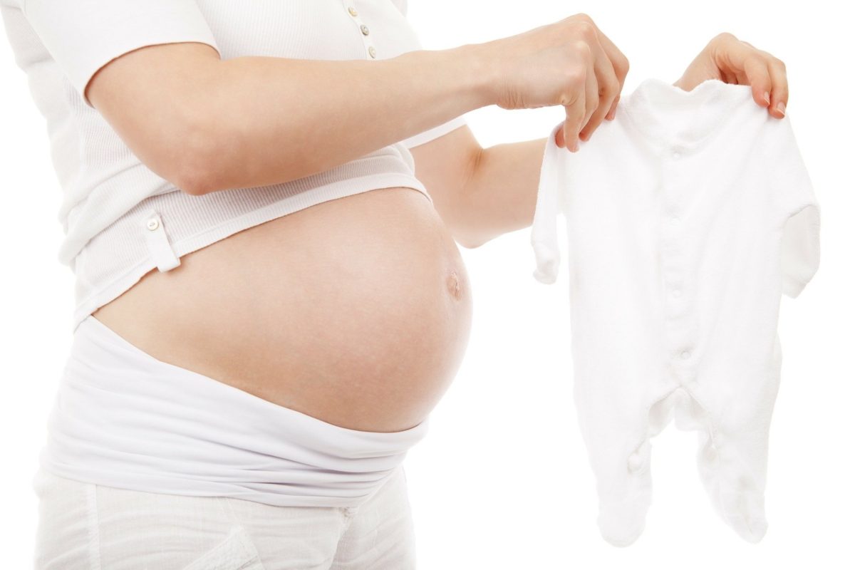 Mujer embarazada sujetando ropa de bebé
